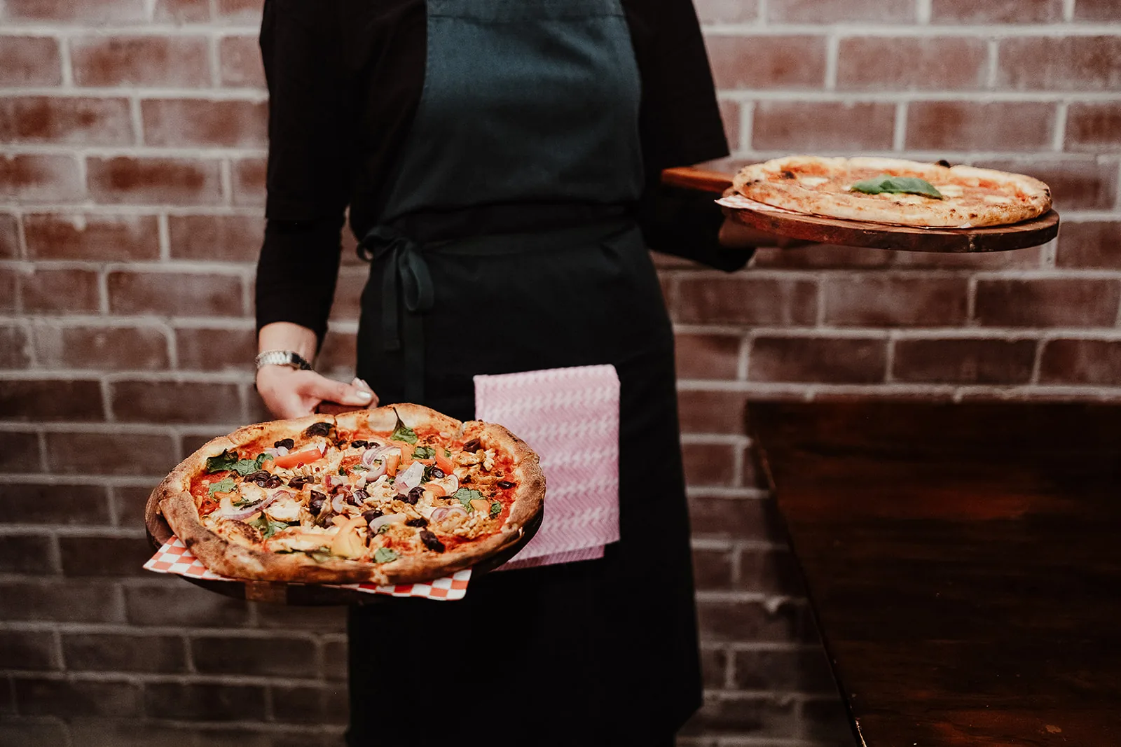 Kickflip Pizza server holding two freshly baked pizzas